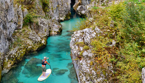 A man stand up paddle boarding on a river, wearing Kokatat gear, that exports its clothing 'made in the USA'